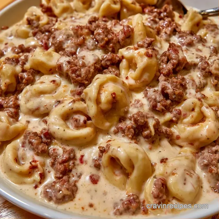 Creamy pasta swirls topped with seasoned beef, garnished with fresh herbs on a minimalist matte black dinner plate.