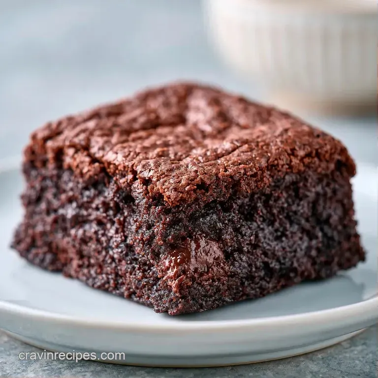 A square of fudgy chocolate cake topped with a dusting of powdered sugar and a fresh mint leaf on a white plate.