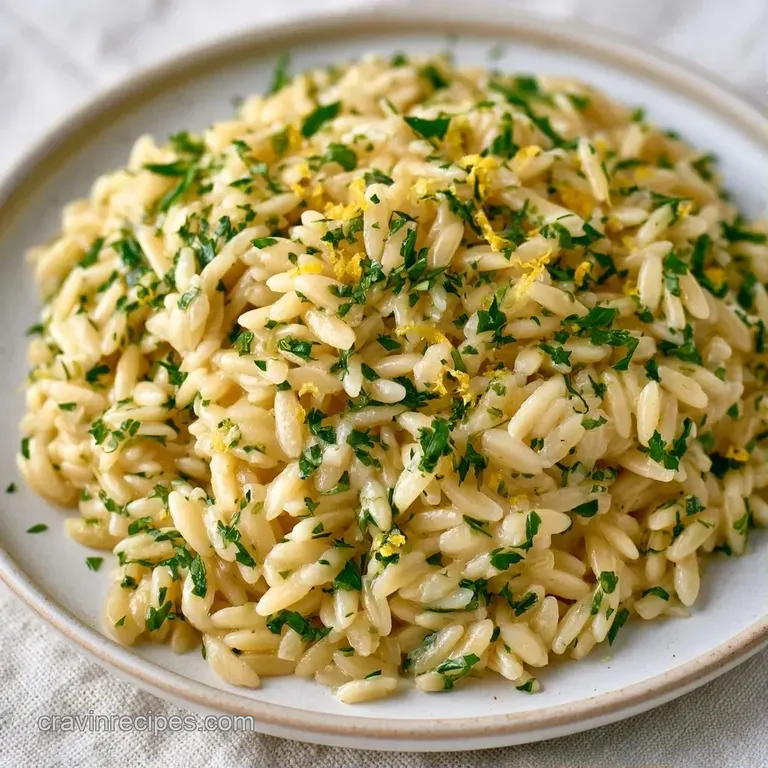 A minimalist plate featuring a mound of buttery pasta topped with a fresh lemon wedge and sprigs of green herbs.